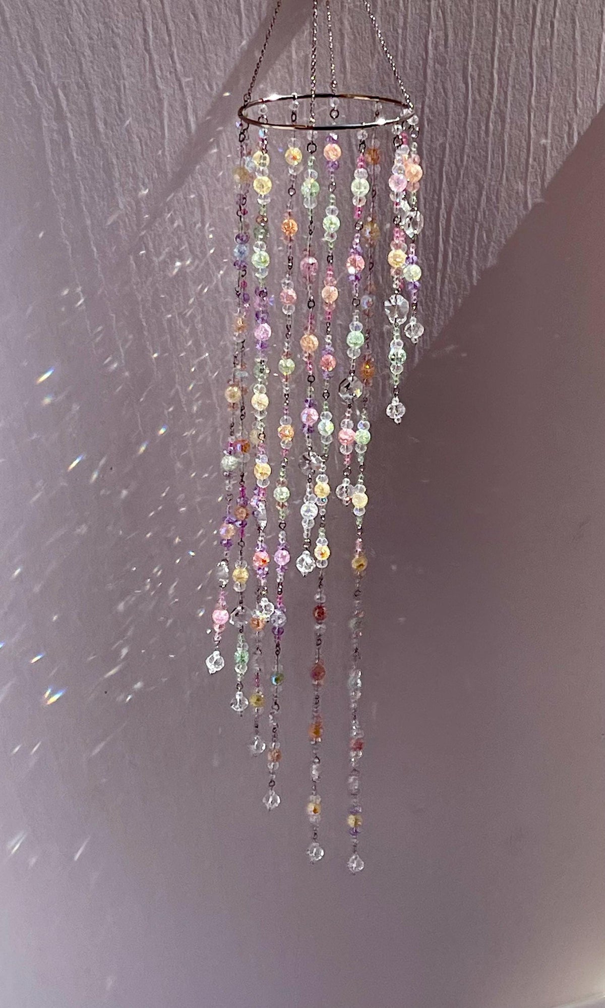 Handmade window suncatcher with colorful glass crystal beads and hanging rainbow-maker prisms arranged in a small curtain design.