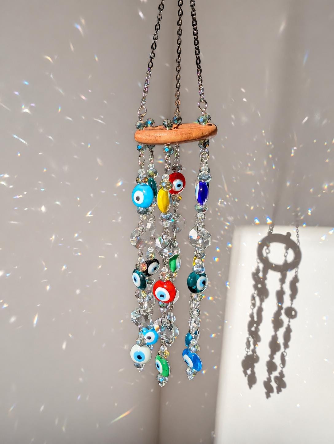 Colorful glass evil eye beads and faceted crystal prisms hanging on metal chains from a natural wooden ring.