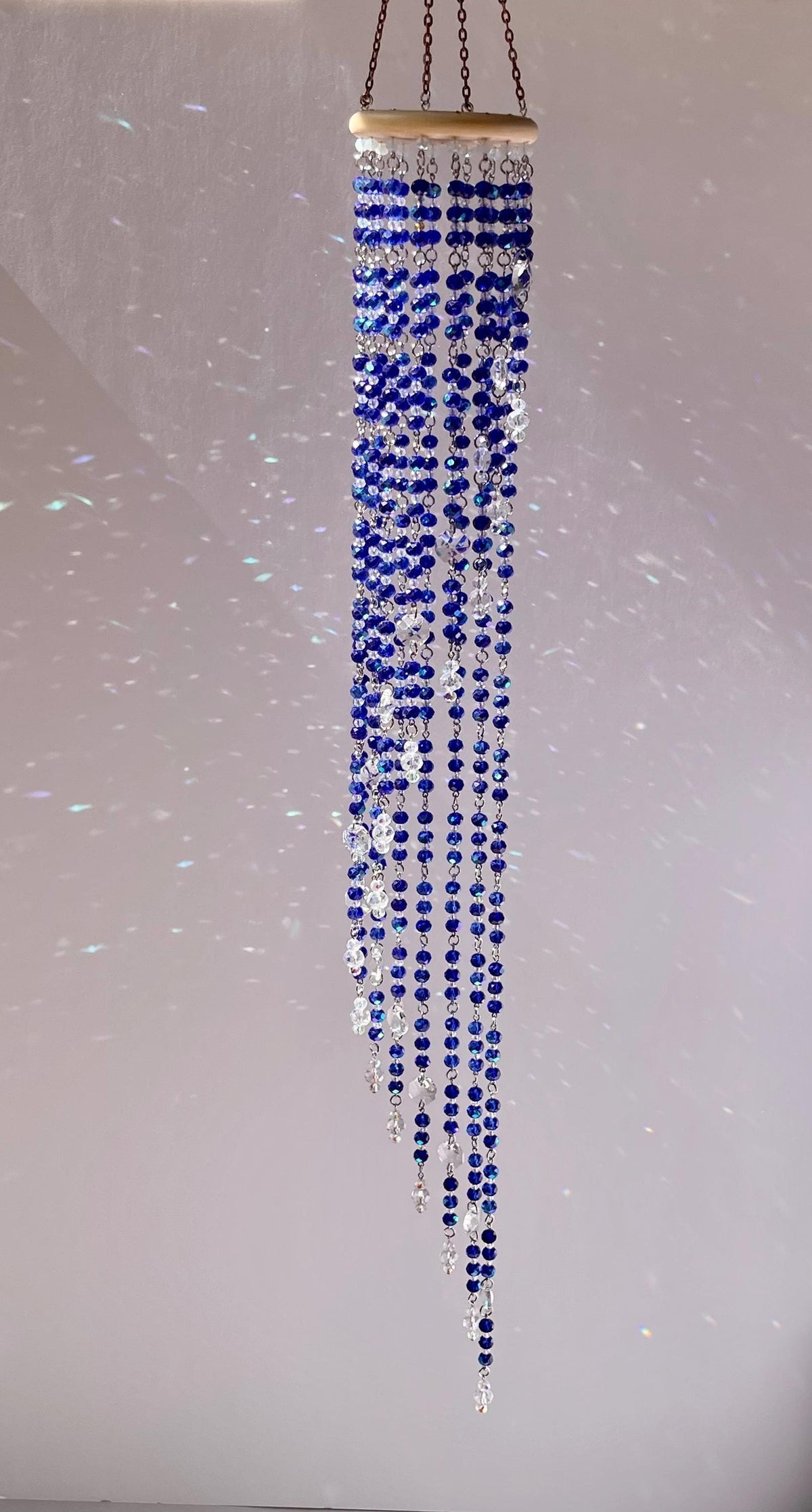 Blue and clear faceted crystal beads cascading in strands of different lengths from a natural wooden ring.
