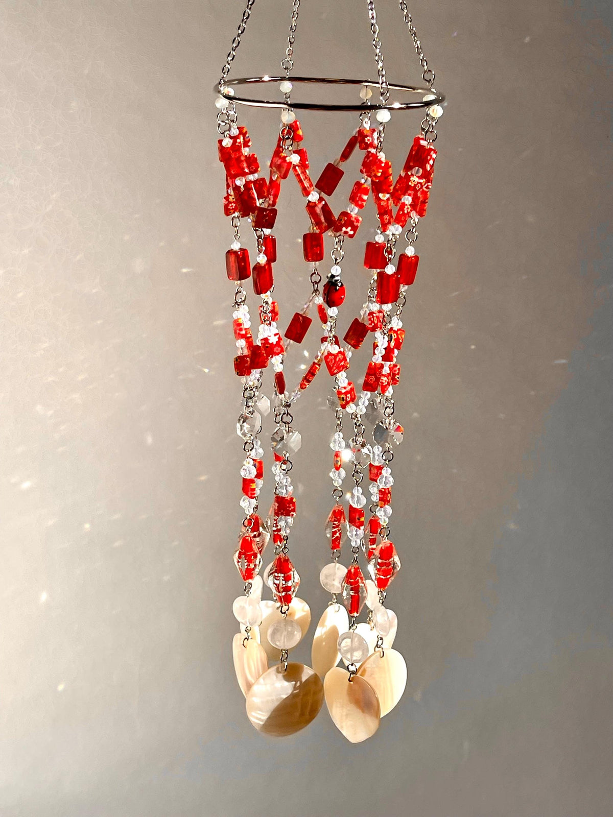 Red glass and Murano bead suncatcher with rainbow-maker crystals, clear quartz and natural seashells suspended from a steel hoop.