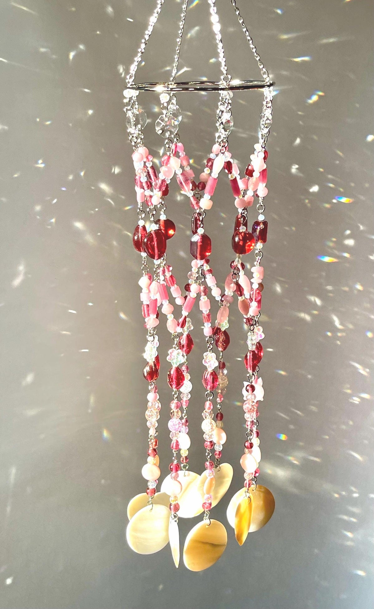 Handmade pink pig suncatcher with pink glass beads, clear flower beads, a glass pig charm and natural seashells hanging from a steel hoop.